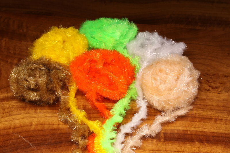 Assorted colors of chenille fly-tying material arranged on a wooden surface.